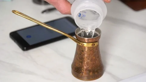 Adding water into copper Cezve Ibrik to make Turkish coffee Stockbeeldmateriaal 123670542