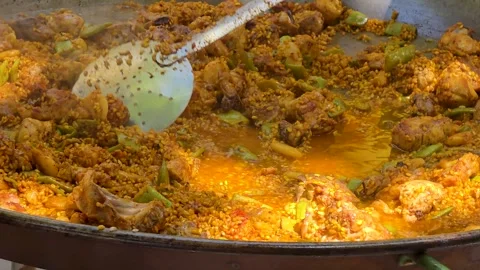 Adding water to fried rice with meat and vegetables in paella pan outdoor co Stock Footage 343796872