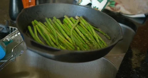 Adding water to a hot frying pan filled with asparagus in slow-motion Stock Footage 149180501