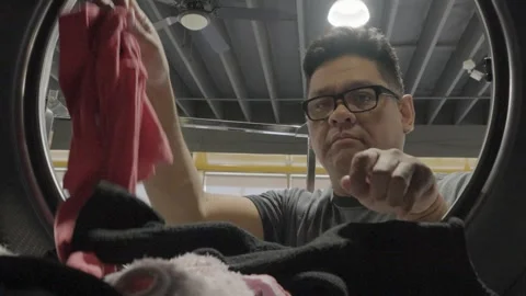 Adding Wet Clothese inside the dryer in the laundry mat Stock Footage 310228404
