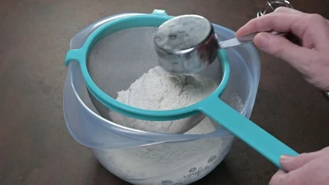 Adding white flour to sieve to sift with steel measuring cup. Male hand Stock Footage 243858722