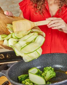 Adding zucchini ribbons to pan Stock Photos