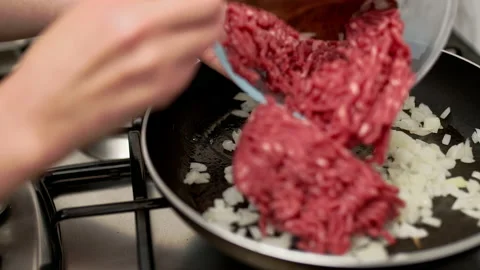 Adding/placing ground beef in a preheated frying pan with chopped onion. Stock Footage 135312818