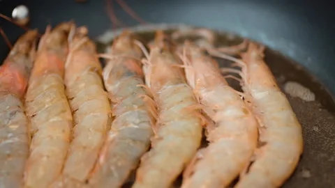 Adding/placing multiple prawns/shrimps in a frying pan with butter and oil in 4K Stock Footage 138286004