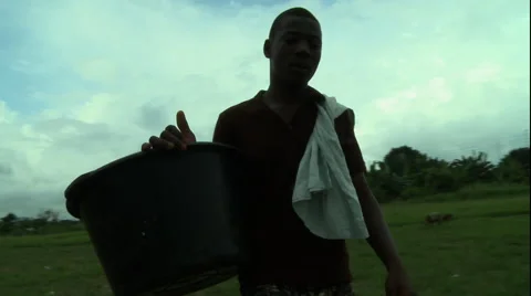 ADEISO BOY WALKS DOWN PATH WITH EMPTY WATER BUCKET Stock Footage 58066338