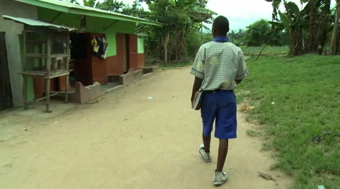 ADEISO STUDENT WALKS DOWN PATH BY BUILDINGS: MOVING SHOT FROM BEHIND Stock Footage 58070064