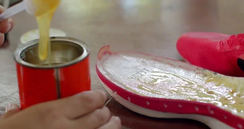 Adhesive is spread evenly on the shoe sole using a stick before pressing it back Stock Footage 313495632