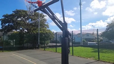 Adjustable basketball net and backboard in sunny public park court with blue Vídeos de archivo 346885456