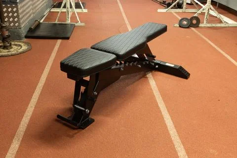 Adjustable exercise bench on a rubberized floor in a well-lit workout area Stock Photos