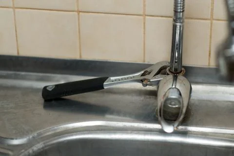 An adjustable spanner lies on a rusty kitchen faucet. Incomplete repair proce Stock Photos