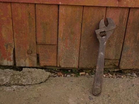 Adjustable wrench with rust leaning against old wooden boards, repair and wea Stock Photos