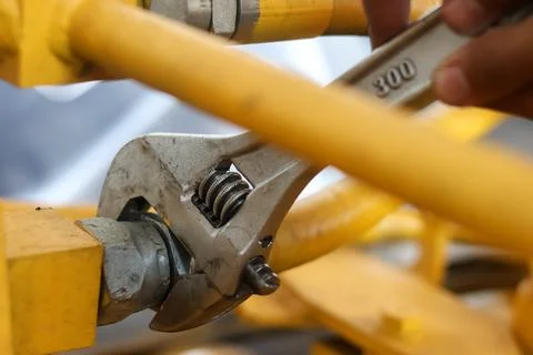Adjustable wrench tightening a pipe fitting on yellow machinery. Stock Photos