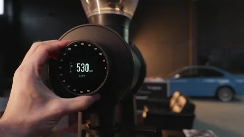 Adjusting coffee grinder settings with blue sports car in background Stock Footage 334732397