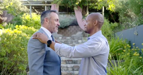Adjusting tie, man on right smoothing collar then hugging partner in garden, Stock Footage 337706341