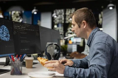 Admin eating croissant while using AI in tech startup office 库存照片