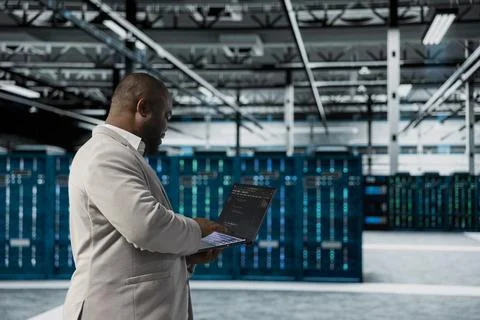 Admin walking in data center running lines of code on laptop Stock Photos