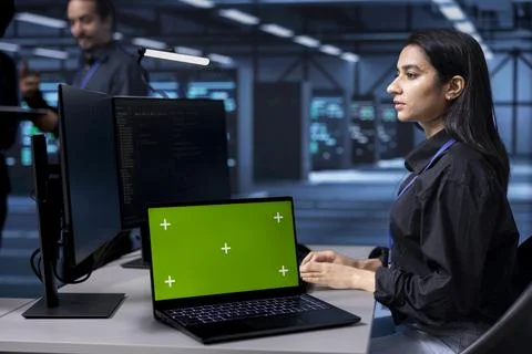 Admin working on green screen laptop in data center housing storage devices Stock Photos