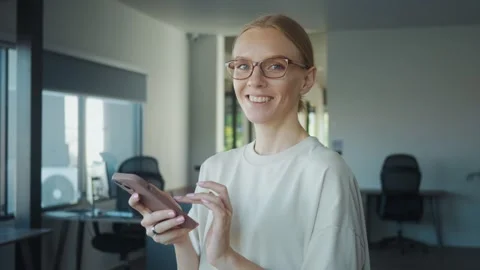 Administrative assistant wearing eyeglasses using mobile phone in modern office Stock Footage 312117987