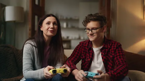 Adolescent boy teaching his mom how to use a game controller, gaming at home Stock Footage 337905748