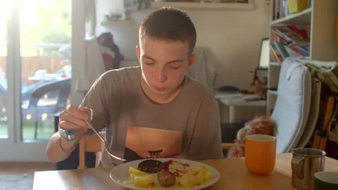 Adolescent sitting at table consuming scrambled eggs and fresh juice Stock Footage 321029368