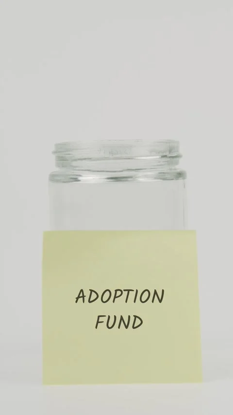 Adoption fund text or word on yellow sticky note attached to glass jar Stock Footage 311675594