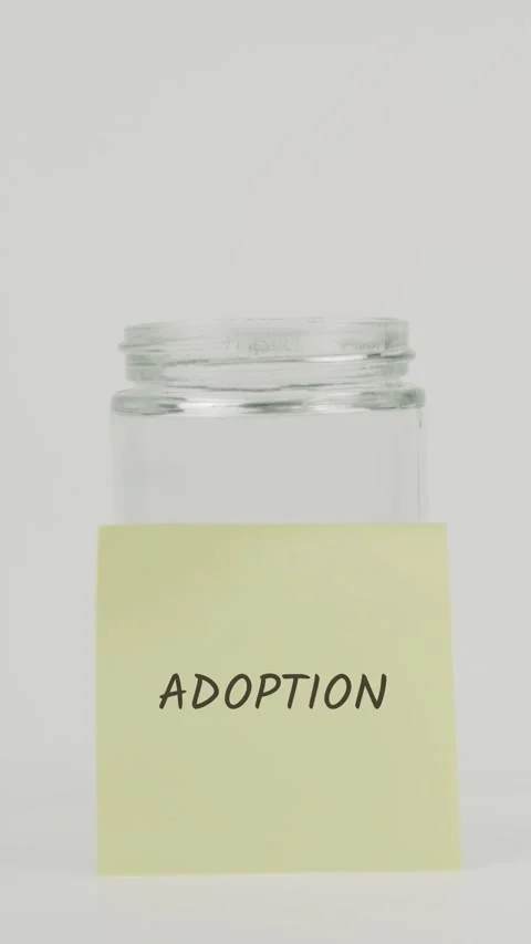Adoption text or word on yellow sticky note attached to glass jar Stock Footage 311675730