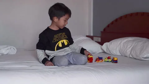 Adorable 4 year boy playing car toy on white bed morning wake up Stock Footage 236738273