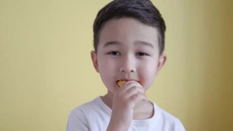 Adorable asian boy eats a piece of nuggets on colour background Stock Footage 195038000