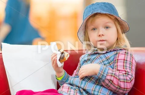 Adorable baby eat donut with chocolate holding it with napkin in mall Stock Photos