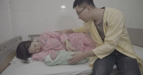 Adorable baby lying on bed surrounded with caring parents in the Maternity ho Stock Footage 127765736
