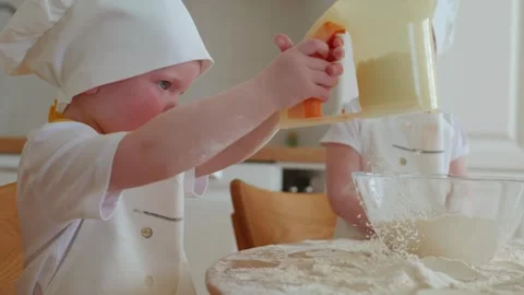 Adorable boy in chefs hat and apron sift flour with a sieve at the kitchen Stock Footage 242194812