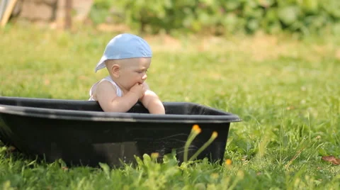 Adorable boy playing with a basin of water in the garden. He gets up and smiles Stock Footage 65093255