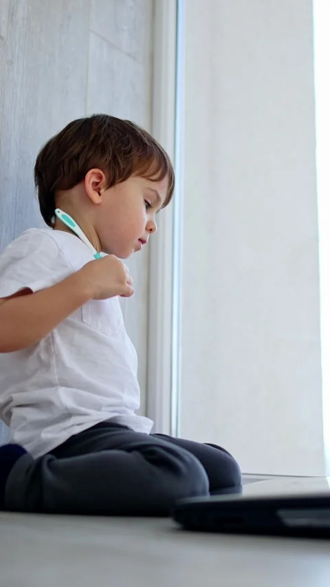 Adorable Caucasian child sits at the panoramic window. Kid looks at laptop in Stock Footage 330239302