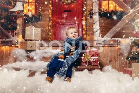 Adorable child boy in winter clothes sits on the porch of the magic house of Stock Photos