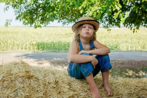Adorable child sits on a haystack Stock Photos