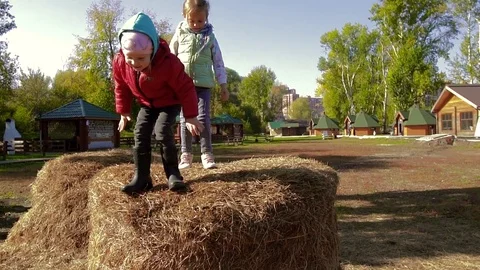 Adorable girl jumping down from haystack, while another girl standing on it Stock-Footage 70825567