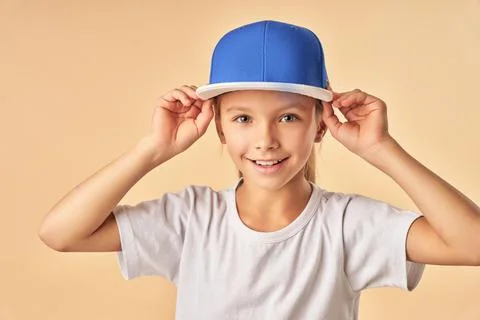 Adorable joyful girl putting on blue baseball cap Stock Photos