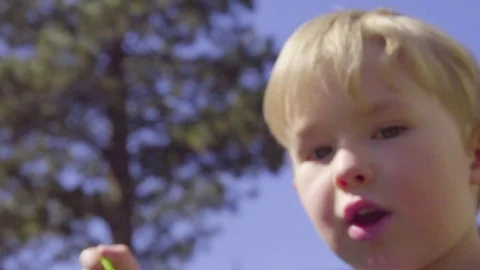 Adorable kid blows bubbles toward camera in extreme close up Stock Footage 75023701