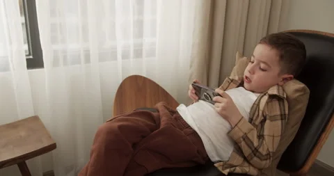 Adorable kid boy playing mobile phone. Handsome boy of 6 years old plays a Stock Footage 236011534