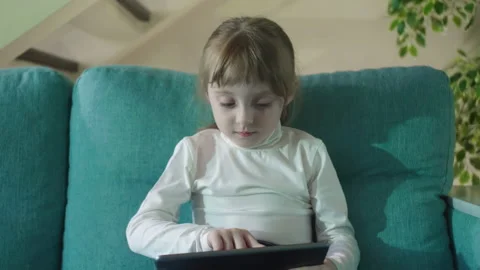 Adorable Kid Girl Using Digital Tablet Watching Cartoons Sitting on Sofa at Home Stock Footage 171784809