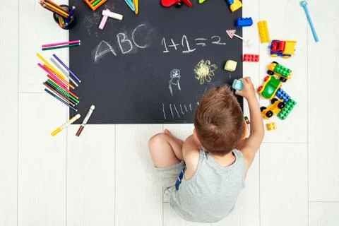 Adorable kid sitting alone using chalk painting on black paper Stock Photos