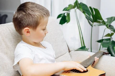 Adorable little boy learning to play acoustic guitar at home. Hobbies and Stock Photos