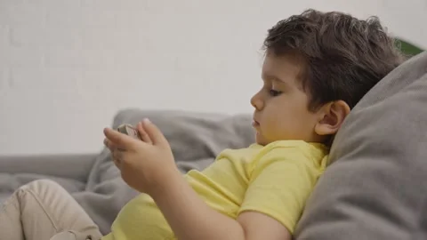 Adorable little boy spending time using tablet phone sitting on sofa at home Stock Footage 247425319
