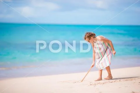 Adorable little girl at beach during summer vacation drawing on sand Stock Photos