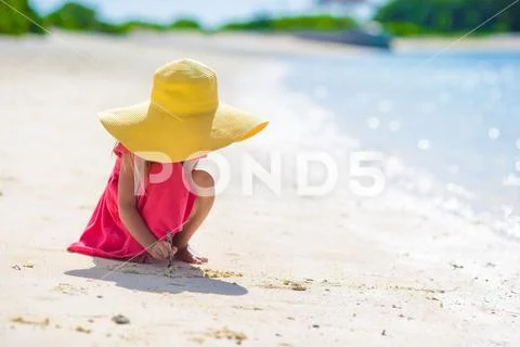 Adorable little girl drawing on white sand at the beach Stock Photos