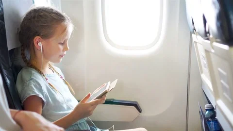 Adorable little girl traveling by an airplane. Cute kid with laptop near window Stock Footage