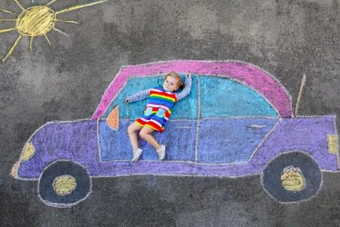 Adorable little toddler girl playing with colorful chalks and painting big car Stock Photos