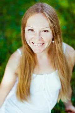 Adorable red-haired smiling young woman sitting on the grass Stock Photos