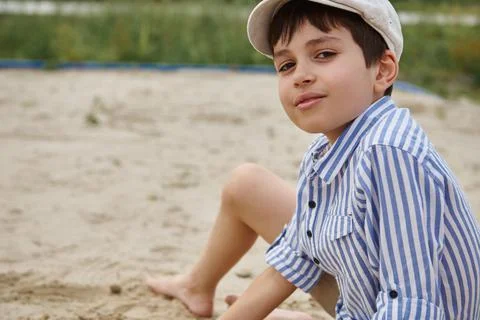 Adorable schoolboy looking at camera while playing on the sand during summer  Stock Photos