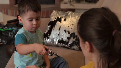 Adorable small boy is playing with a toy bike while mother is watching him on Stock Footage 154113208
